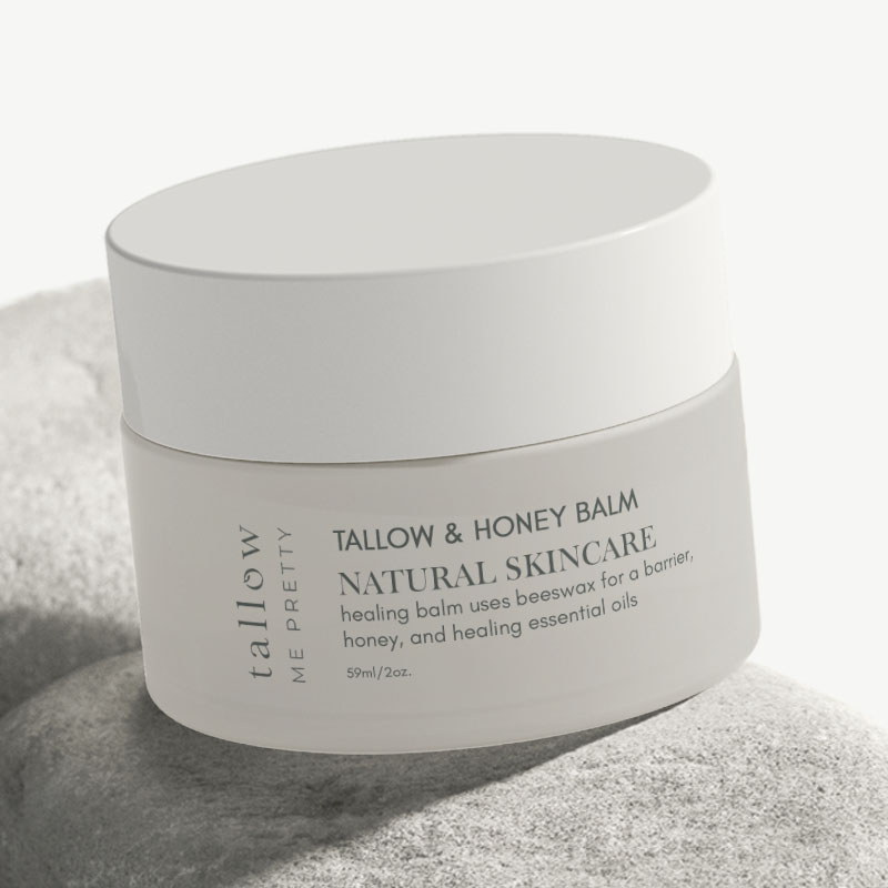 A detailed view of a tallow and honey balm jar on a stone, emphasizing the clean typography and soft color palette.